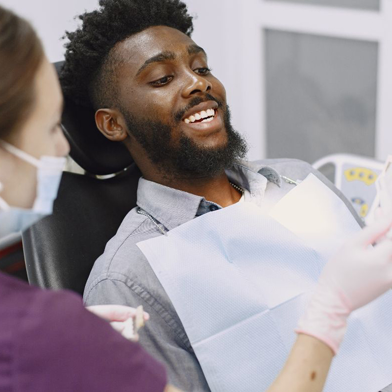 Black male patient sitting in a dental chair receiving treatment smiling